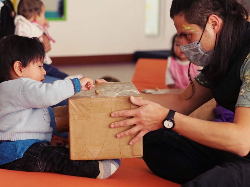 Niño jugando con una caja y un artista del Programa Nidos