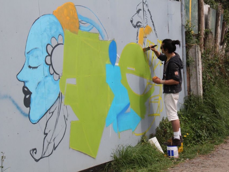 Hombre pinta con brocha un mural en el exterior de día
