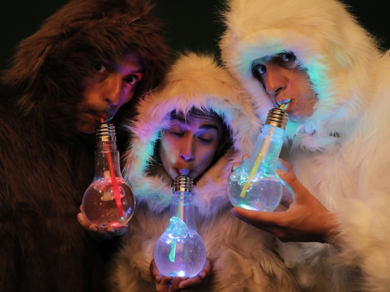 Tres artistas con trajes completos de peluche beben agua de unos bombillos a través de pitillos