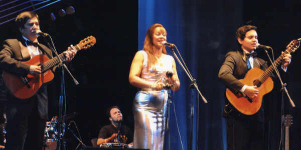Dos hombres con guitarra y mujer cantando en el escenario