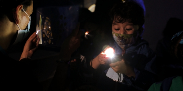 Niño jugando con una linterna y con una artista comunitaria