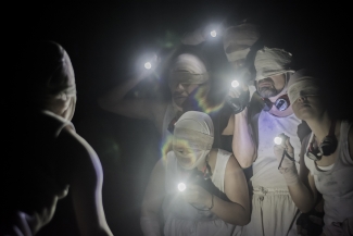 Grupo de actores con los ojos vendados y luces de linterna.