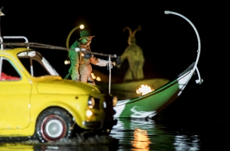 Actores con auto amarillo y góndola verde sobre el lago.