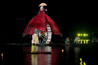 Marioneta gigante sobre rueda y actores en el lago.