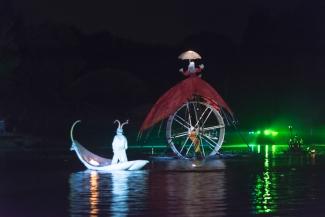 Mujer sobre rueda gigante y actor en góndola blanca sobre el lago.