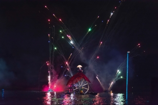 Mujer sobre rueda gigante y luces de colores sobre el lago.